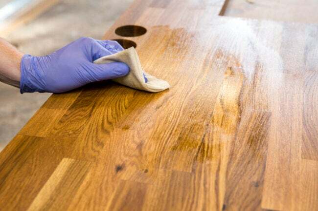 кокосова олія використовує ручне витирання дерев’яної поверхні клейонкою в фіолетових рукавичках