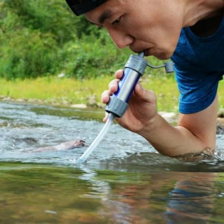 Bărbat care folosește filtrul de apă pentru a bea din pârâu