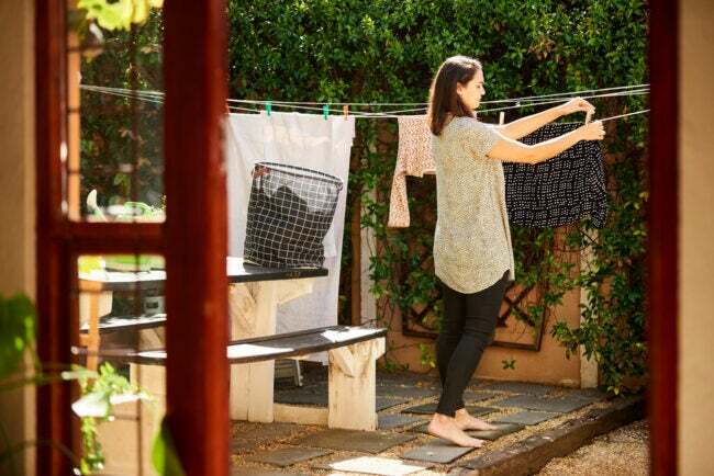 A mulher pendura a roupa no varal no quintal na luz brilhante da manhã
