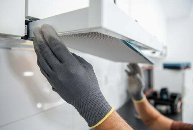 nærbillede af emhættefilter, der fjernes med to hænder med grå handsker