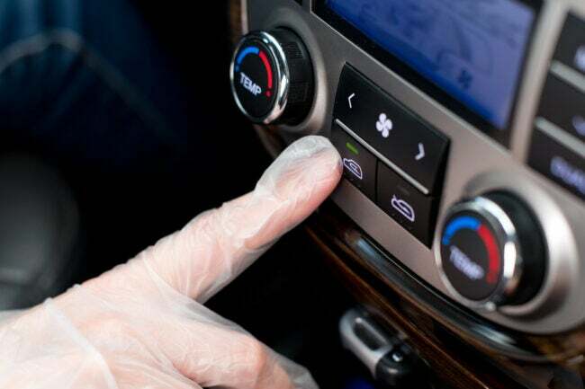 医療用手袋をはめた手が車内の空気循環ボタンを押す