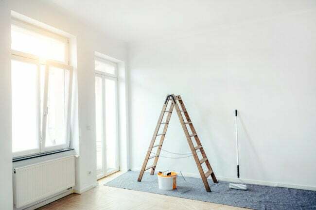 valkoinen huone, jossa tikkaat ja maalaustarvikkeet, joissa auringonvalo virtaa avoimesta ikkunasta