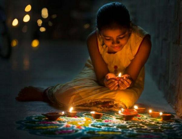 o-fată-ține-a-aprins-diya-și-o așează-pe-un-rangoli-pentru-sărbătoarea-diwali