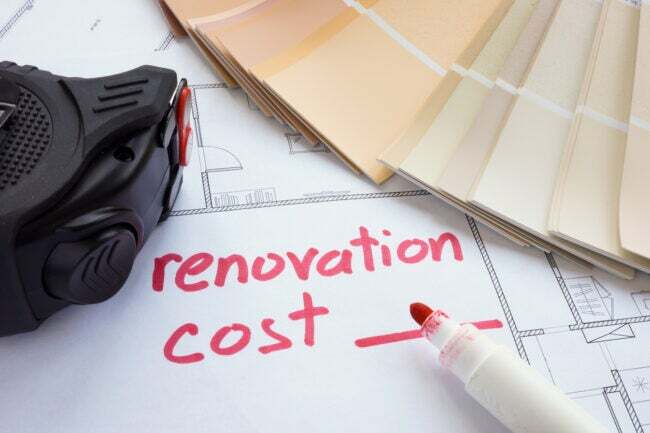Vārdi “renovācijas izmaksas” ir rakstīti sarkanā krāsā uz mājas plāna ar paraugiem un mērlenti, kas atrodas blakus.
