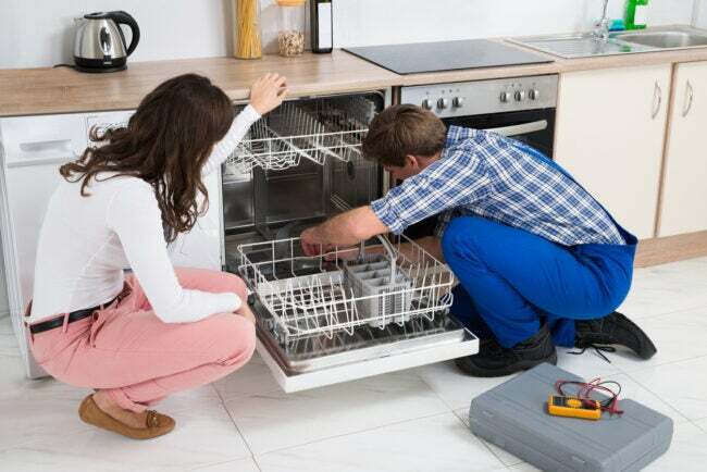 Jauna sieviete skatās uz remontētāju, kas remontē trauku mazgājamo mašīnu virtuvē