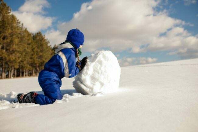 Un niño haciendo una base de muñeco de nieve en la nieve fresca