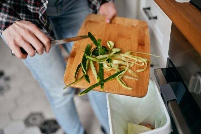 महिला रसोई में सब्जियों के बचे हुए टुकड़ों को ऑर्गेनिक रीसाइक्लिंग और कंपोस्टिंग बिन में डाल रही है।