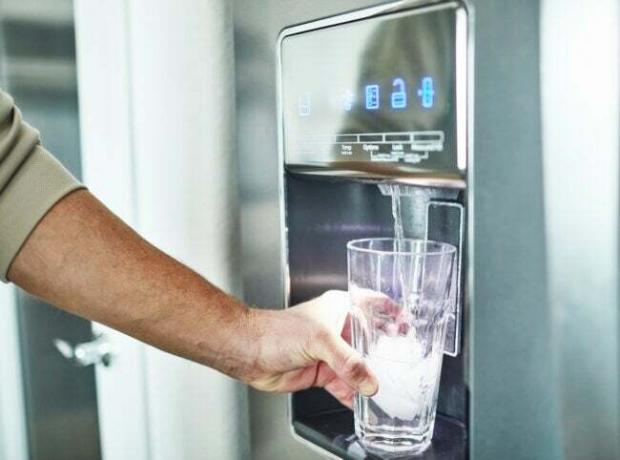 iStock-1300229763 不動産業者は、冷蔵庫のウォーター ディスペンサーからグラスを満たす男性を望んでいません。