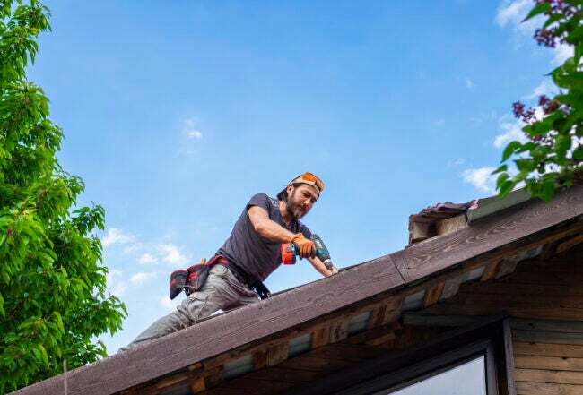Muž pracující na střeše pomocí elektrického šroubováku.