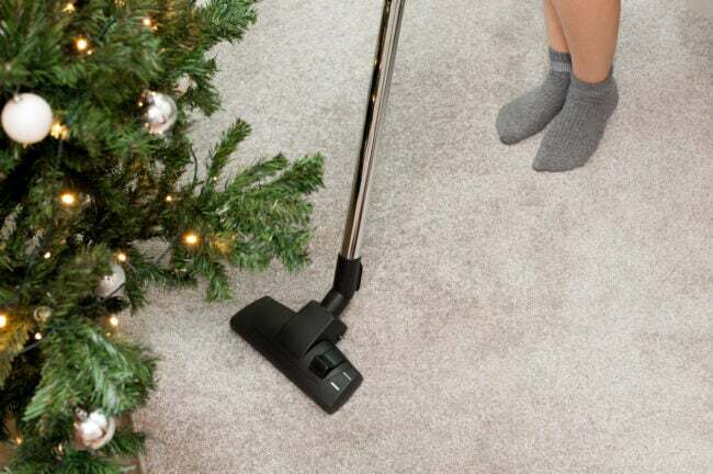 Person som använder en stavdammsugare för att rengöra mattan nära en julgran.