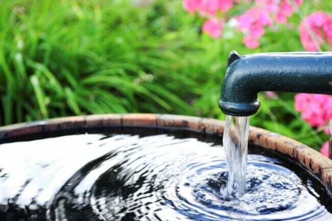 Una pompa dell'acqua in giardino che riempie un barile.