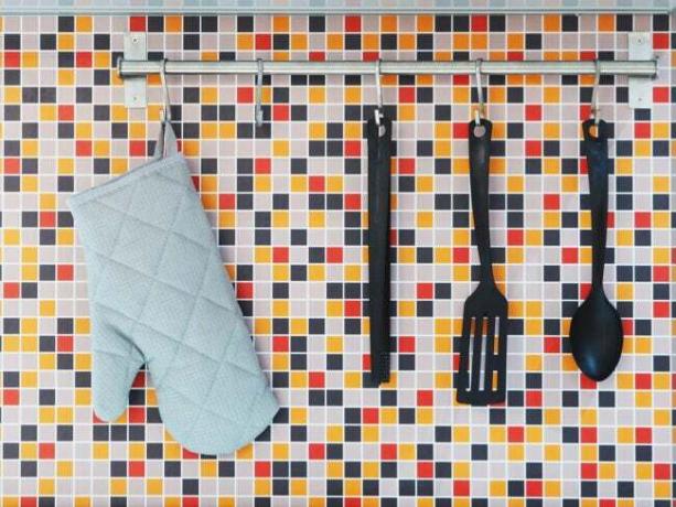 Schwarze Küchenutensilien hängen neben blauem Ofenhandschuh vor bunt gefliester Küchenwand