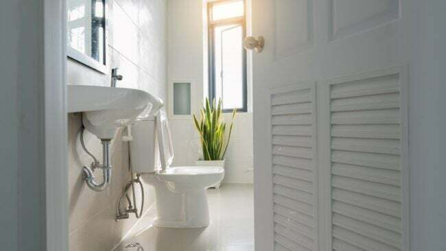 Baltos žaliuzės durys, atsiveriančios į švariai baltą vonios kambarį.