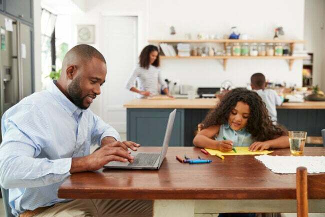 homem na cozinha com a família fazendo pesquisas no laptop com a filha na mesa