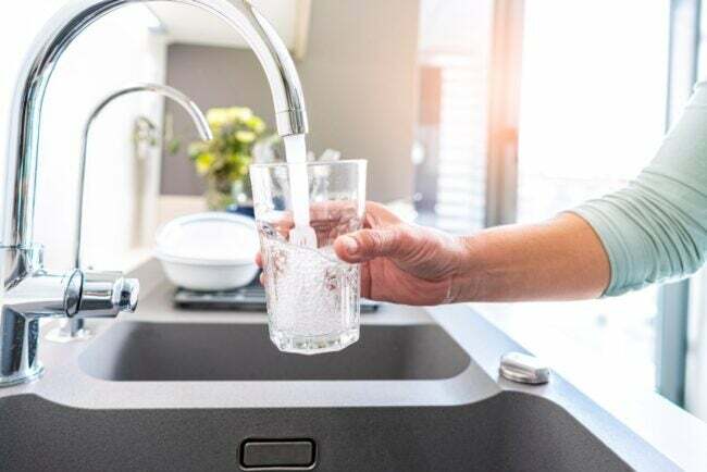 Una persona che riempie un bicchiere d'acqua dal rubinetto del lavello della cucina.