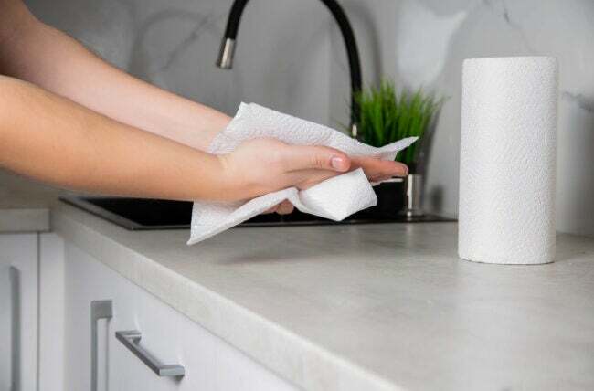 Hände mit Papiertuch neben dem Waschbecken mit Handtuchrolle auf der Küchentheke abwischen