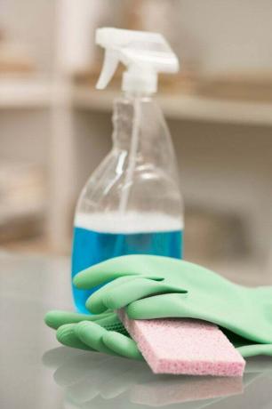 Sprühflasche mit blauer Reinigungslösung im Inneren, Handschuhe und Schwamm und verschwommener Hintergrund auf der Theke