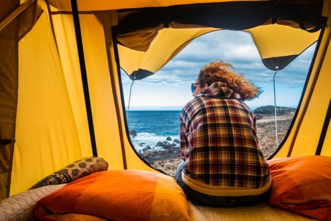 Жена у жутом камперском шатору гледа у океански пејзаж