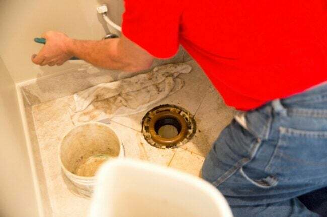 Encanador substituindo um flange de vaso sanitário em um banheiro.