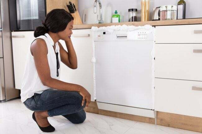 Mulher chateada com a máquina de lavar louça transbordando