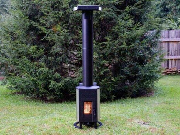 Ψηλό, μαύρο Solo Stove Tower Patio Heater στο γκαζόν μπροστά από ένα αειθαλές δέντρο.