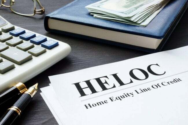 「HELOC ホームエクイティ信用枠」という言葉が書かれた文書が、ペン、本、お金、メガネ、電卓とともにテーブルの上に置かれています。