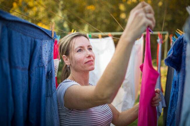 Nainen ripustaa kirkkaita vaatteita pyykkinarulla ulkona