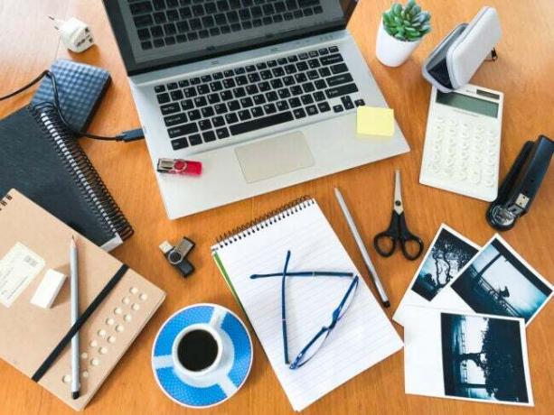 skrivbord i ljust trä täckt med kaffekoppar för laptop dagliga planerare fotografier och andra kontorsmaterial