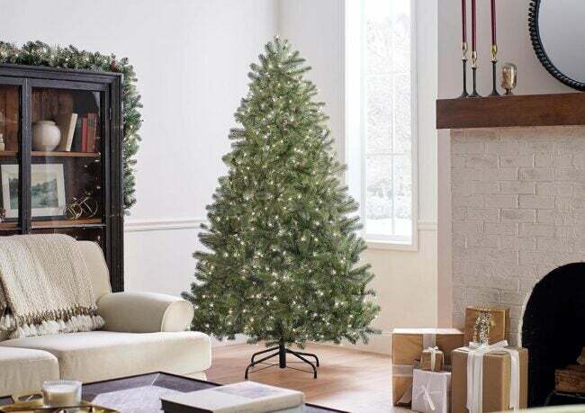 The National Tree Company Full Downswept juletræ i en neutral stue ved siden af ​​en muret pejs med indpakkede gaver.